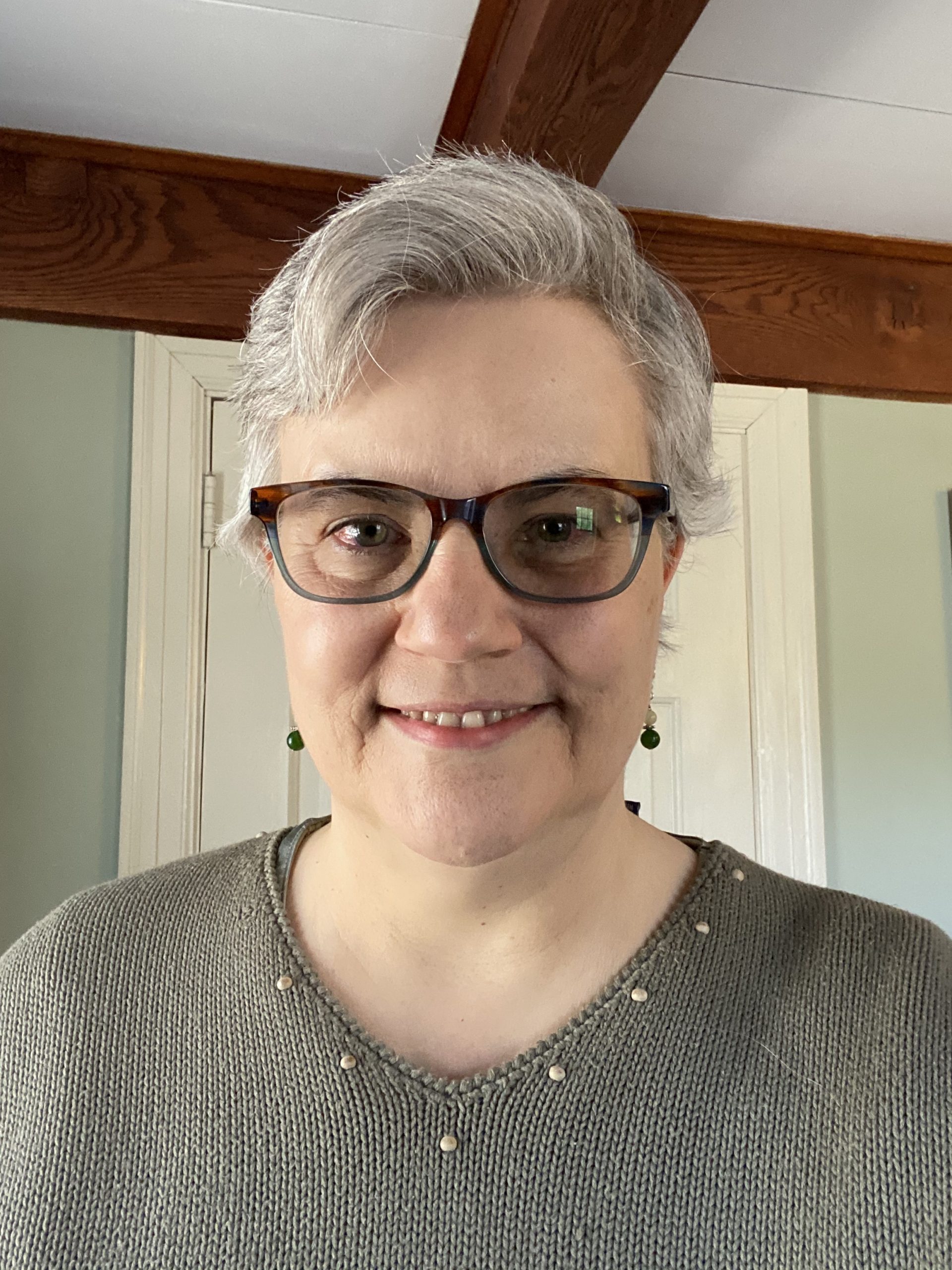 Woman with grey hair and glasses wearing a green top